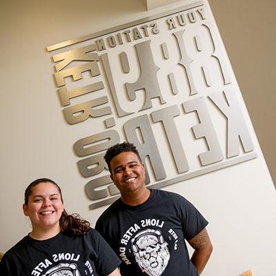 Two students taking a picture infront of the 88.9 KETR radio sign.